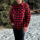 A man wearing a red and black buffalo check flannel shirt with two flap breast pockets and a button cuff, standing outdoors.