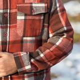 Close-up of a red and brown plaid shirt with a blurred natural background