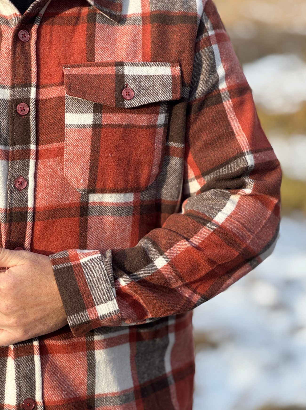 Close-up of a red and brown plaid shirt with a blurred natural background