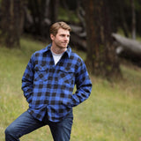 A man wearing a royal blue and black buffalo check padded flannel camping outdoor jacket with jeans.