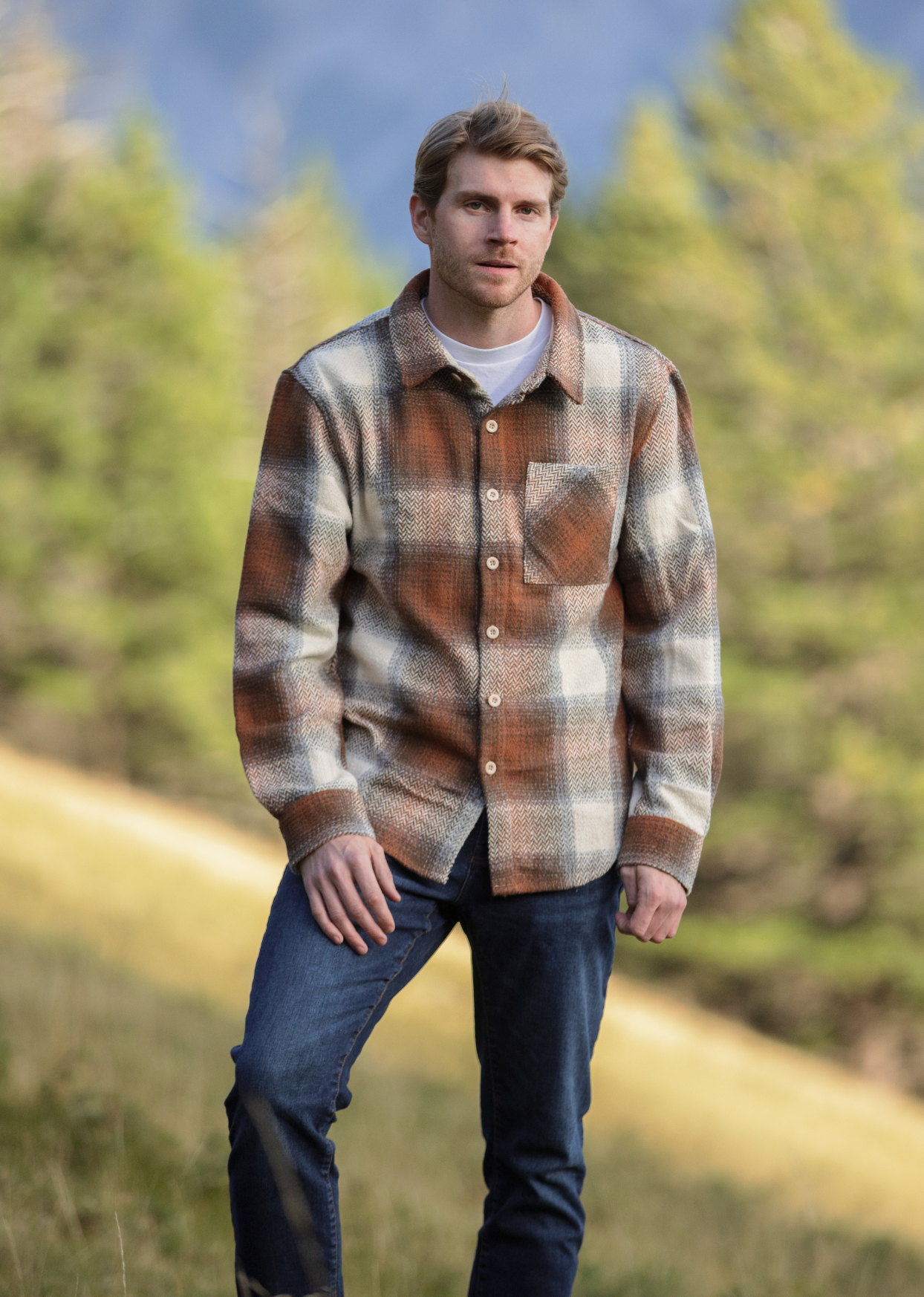 A person standing outdoors wearing a plaid flannel jacket with a herringbone weave in a blend of brown and grey tones, buttoned at the cuffs and chest.
