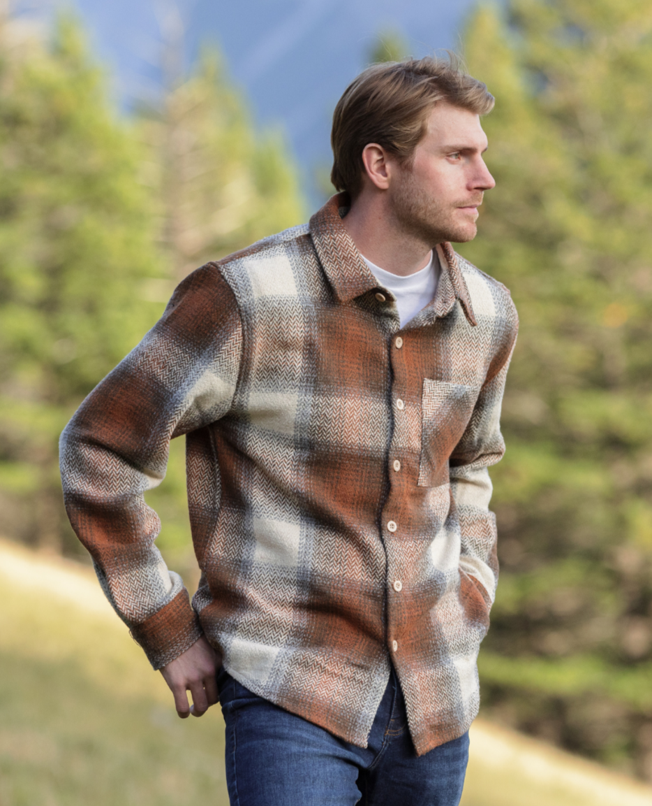 Man standing wearing our Sand Wool jacket, hands in back pockets, trees in the background