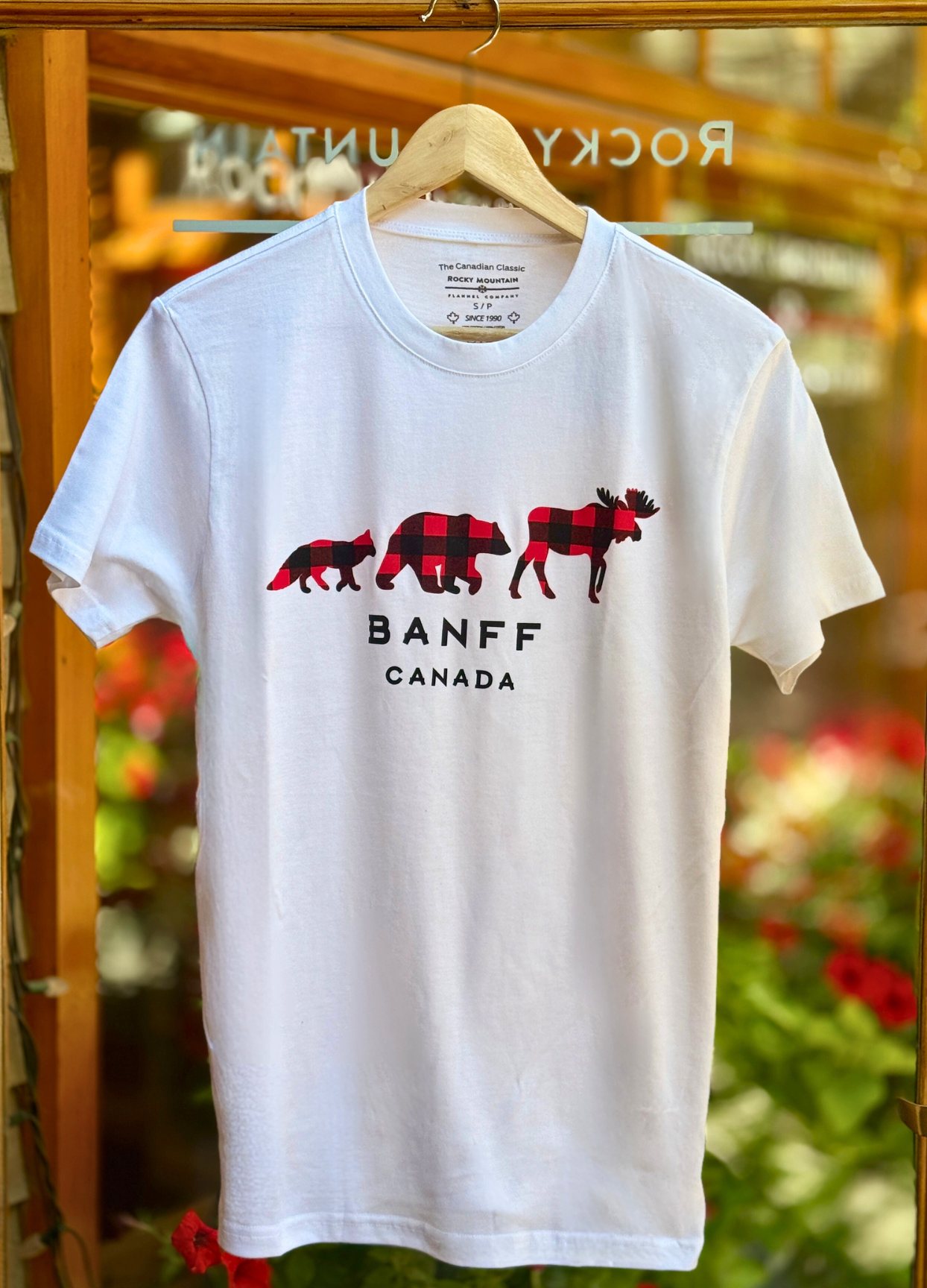White t-shirt with red plaid bear design and 'Banff Canada' text on a hanger.