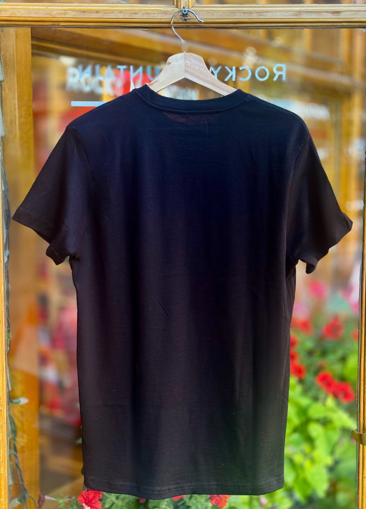 Black t-shirt on a hanger with a blurred store and floral background