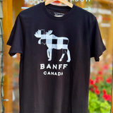 Black t-shirt with moose graphic and 'Banff Canada' text on a hanger in front of a store entrance.