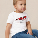 A toddler boy wearing a white short-sleeve t-shirt with a red and black moose graphic and the text 'BANFF CANADA', paired with blue jeans, sitting against a plain beige background.