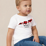 A toddler boy wearing a white short-sleeve t-shirt with a red and black moose graphic and the text 'BANFF CANADA', paired with blue jeans, sitting against a plain beige background.