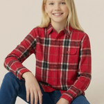 Child wearing a red plaid shirt and blue jeans sitting on a white surface with a beige background