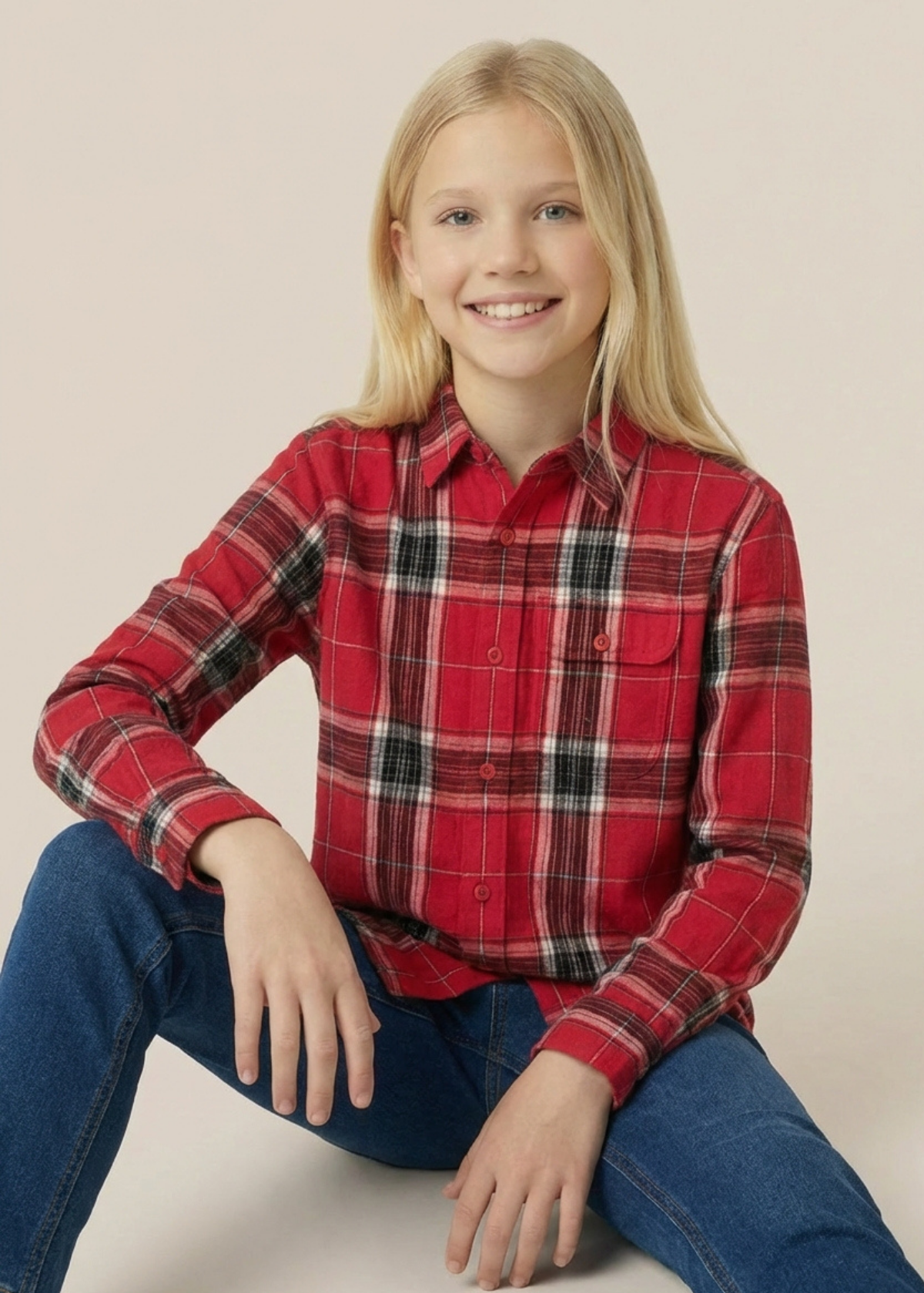 Child wearing a red plaid shirt and blue jeans sitting on a white surface with a beige background