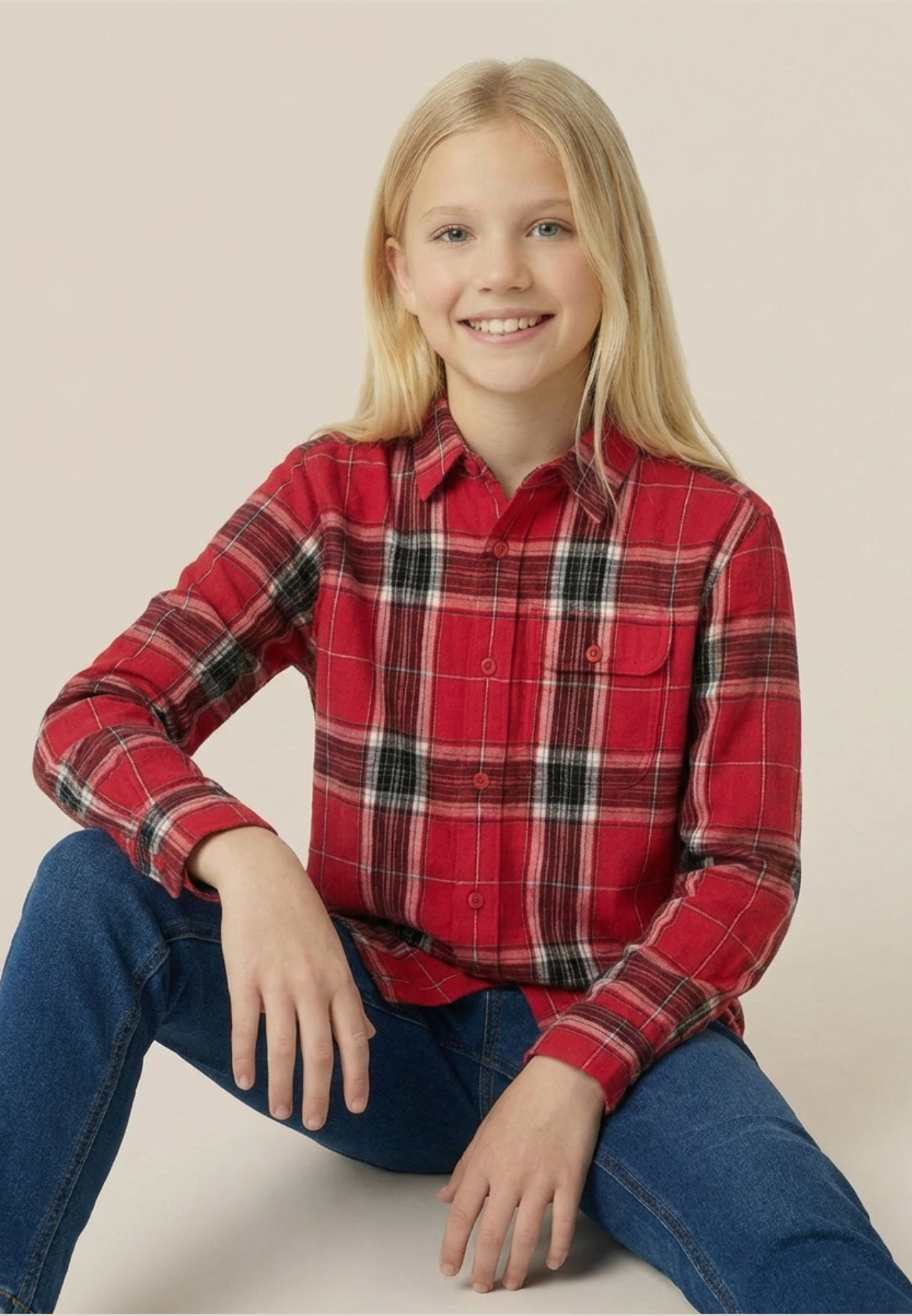 Child wearing a red plaid shirt and blue jeans sitting on a white surface with a beige background