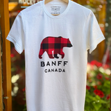 White t-shirt with a bear graphic and 'Banff Canada' text on a hanger against a blurred background.