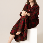 Woman wearing a red and black plaid nightshirt sitting on a white stool against a beige background