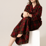 Woman wearing a red and black plaid nightshirt sitting on a white stool against a beige background