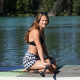 A girl paddle boarding wearing black and white buffalo check shorts