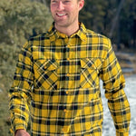 A man wearing a long-sleeved yellow and black flannel plaid shirt with two flap breast pockets and a button cuff.