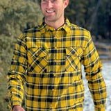 A man wearing a long-sleeved yellow and black flannel plaid shirt with two flap breast pockets and a button cuff.