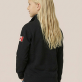 Person wearing a black jacket with a flag patch on the back against a beige background