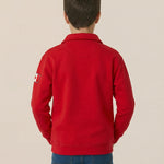 Person wearing a red jacket with a logo on the back against a beige background