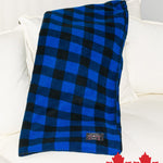 A blue and black checkered fleece blanket laid out on a white sofa, with a small branded tag visible.