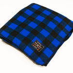 A blue and black checkered fleece blanket laid out on a white background, with a small branded tag visible.